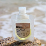 Hanky Planty Petite Antibacterial Body Wash, Mangosteen scent, 30ml refill pouch with brown label, placed on a rock by the beach with waves in the background.