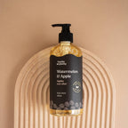 Hanky Planty Watermelon & Apple natural body wash, 500ml pump bottle with black label and golden liquid, placed on an arched wooden board against a beige background.
